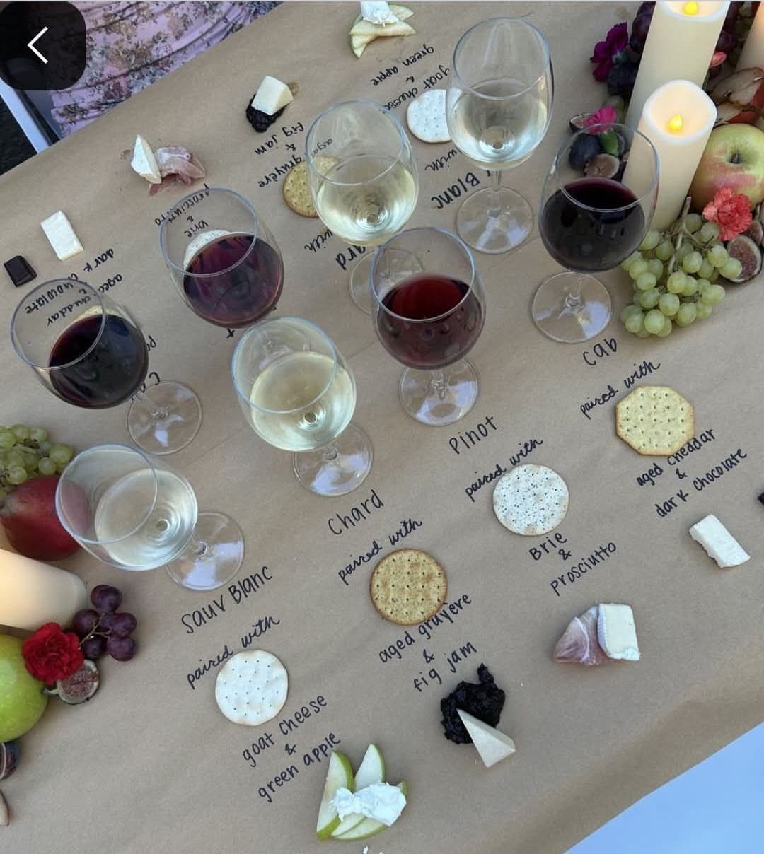 Wine tasting setup with red and white wine, cheese, crackers, and fruit pairings.