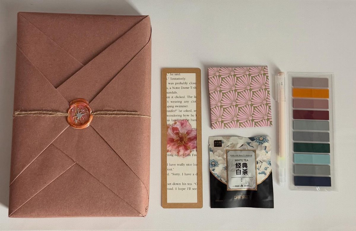 Wrapped gift with wax seal, bookmark, tea, and pen on white background