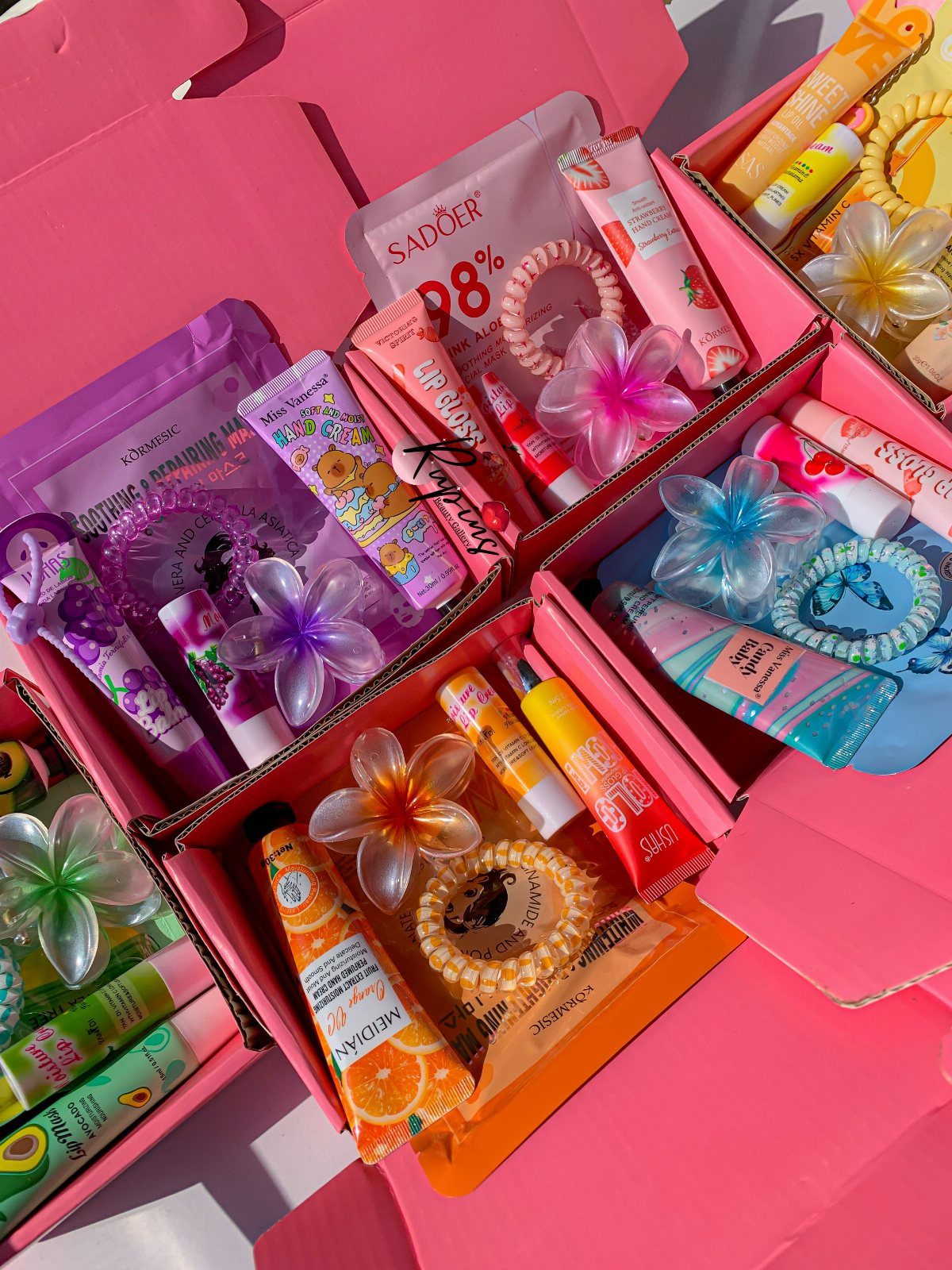 Assorted beauty products and hair accessories packed in several pink gift boxes.