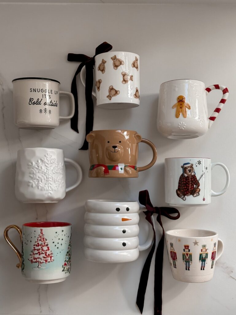 Assorted Christmas themed coffee mugs with festive designs and black ribbons on white background