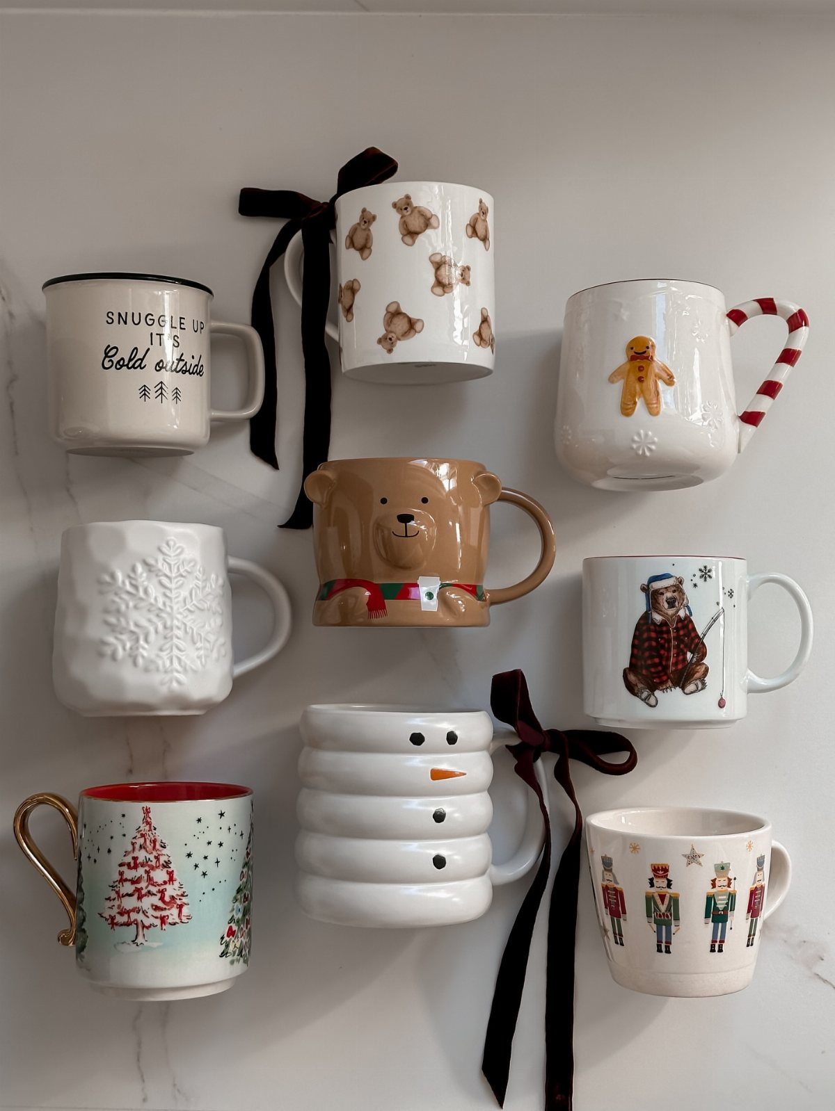 Assorted Christmas themed coffee mugs with festive designs and black ribbons on white background