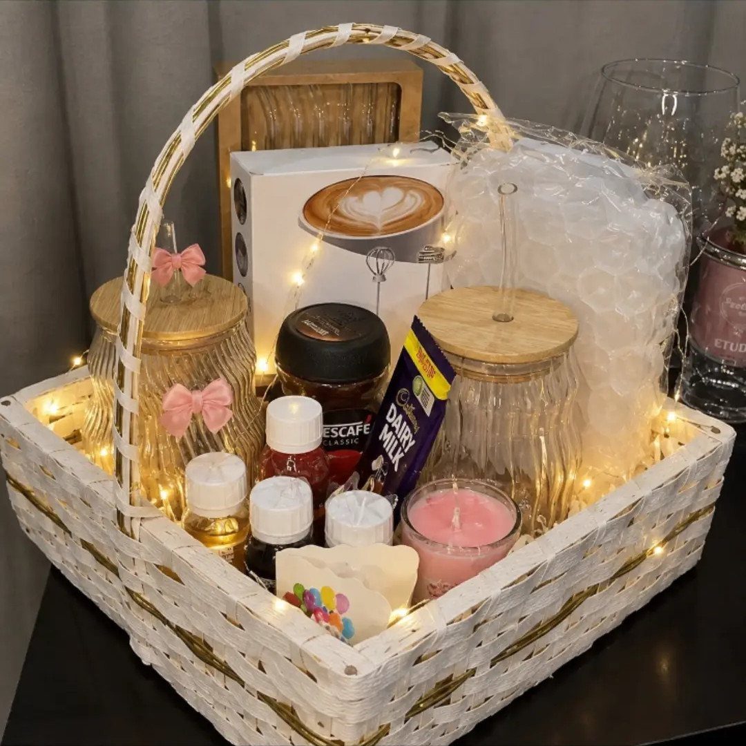 White woven gift basket filled with coffee, chocolate, candles, and warm fairy lights.