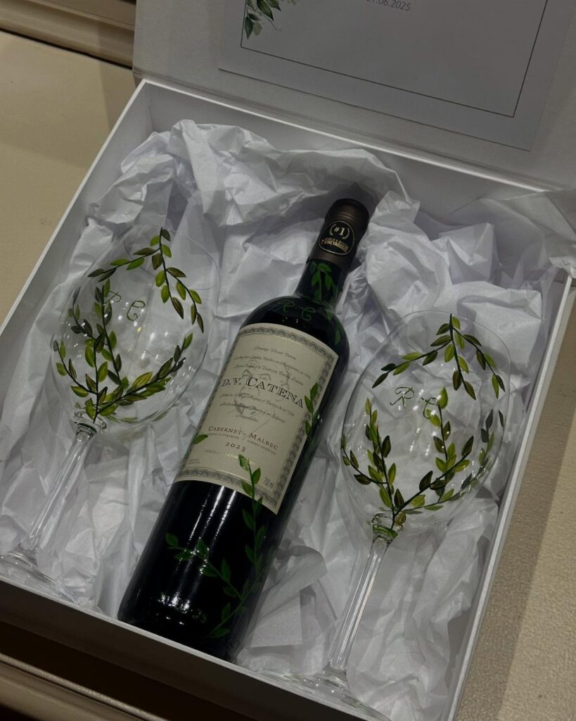 Bottle of red wine and two leaf-patterned glasses in a white gift box.