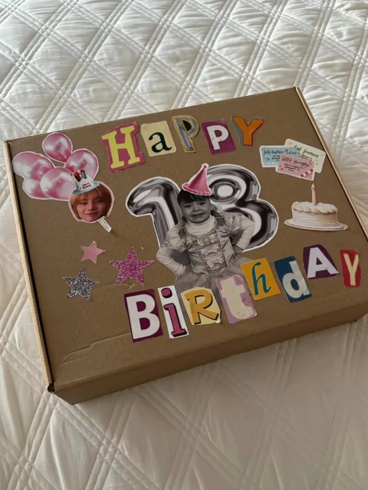Decorated birthday gift box with colorful letters, photos, and stars on white bedding
