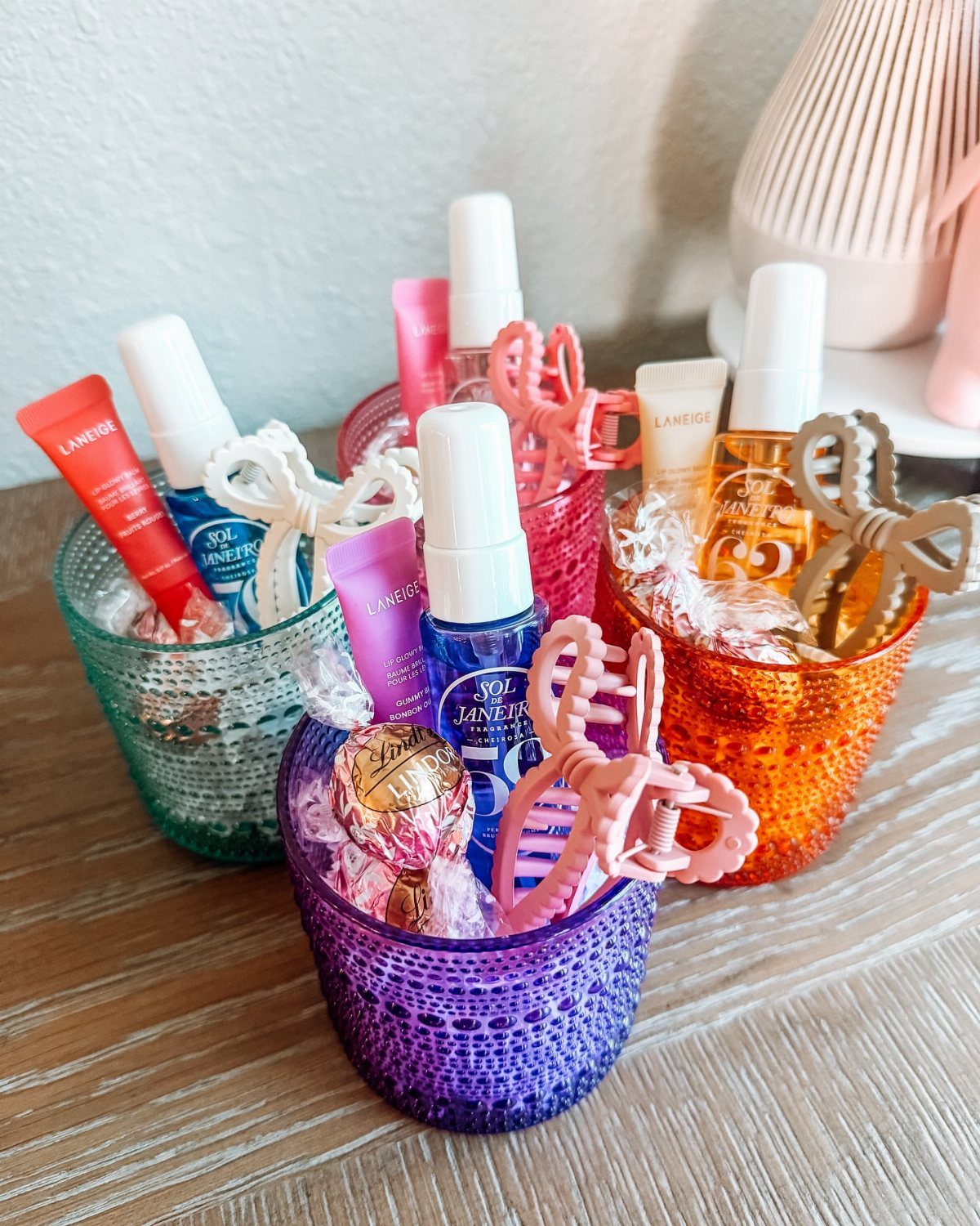 Colorful glass cups filled with beauty products and chocolates as gift sets.