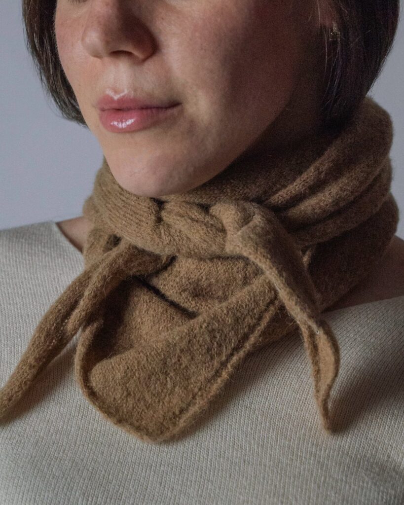 Brown textured wool scarf tied around a woman's neck over a cream top.
