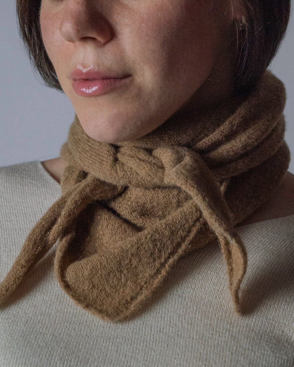 Brown textured wool scarf tied around a woman's neck over a cream top.