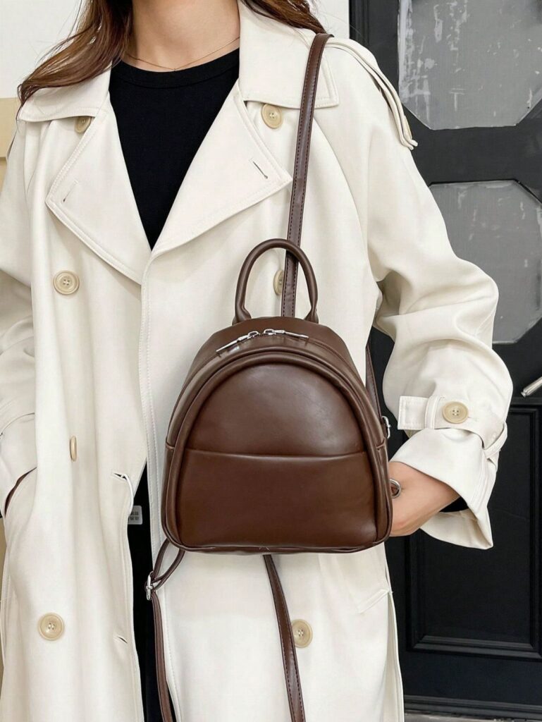 Brown leather mini backpack worn by a person in a white trench coat.