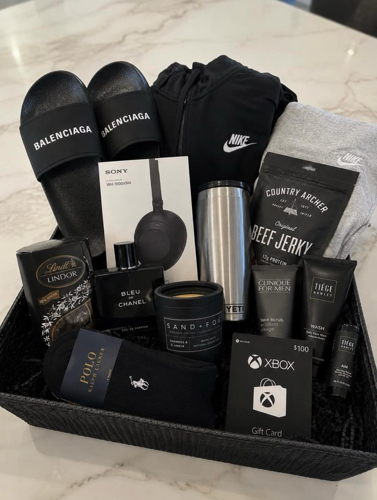 Gift basket containing luxury slides, electronics, cologne, and snacks for a man.