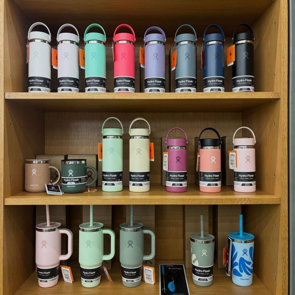 Hydro Flask water bottles and tumblers in various colors on a wooden shelf.