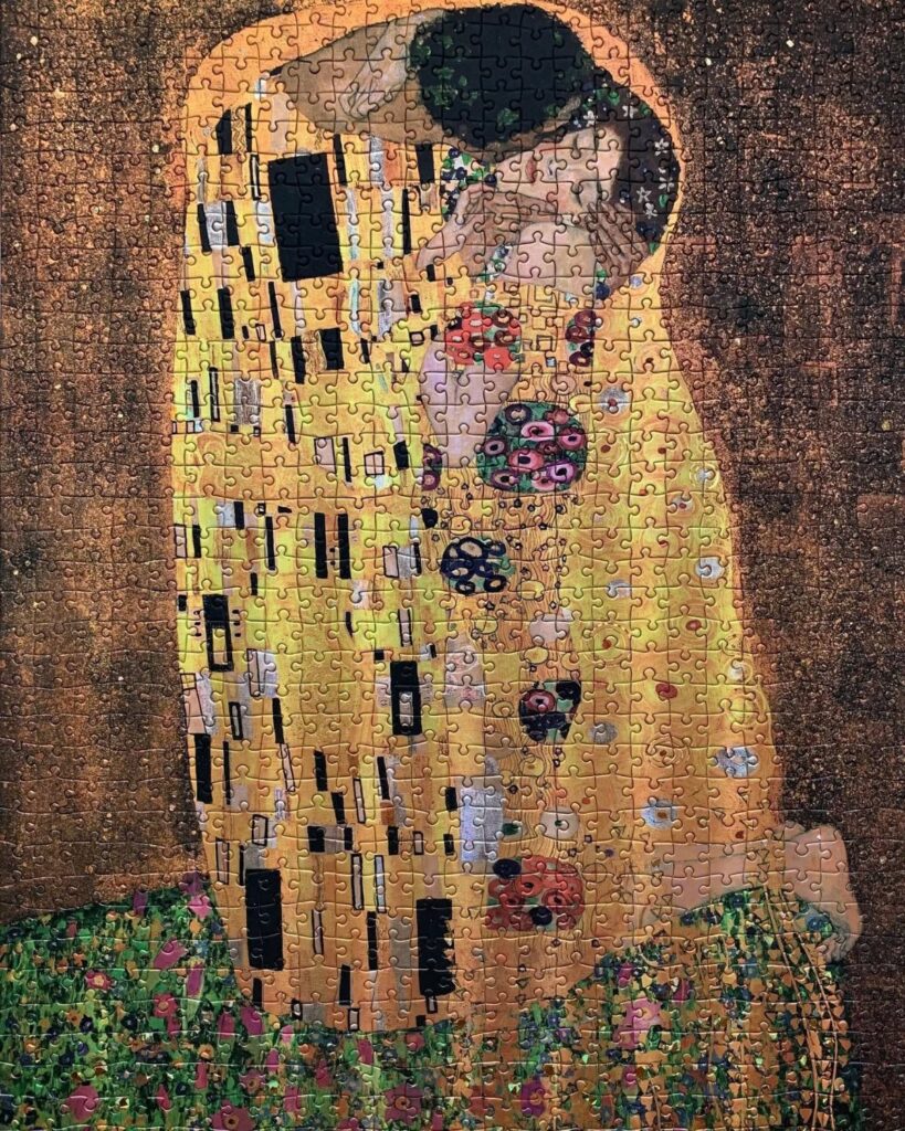 Jigsaw puzzle of Gustav Klimt's The Kiss featuring gold-patterned figures embracing.