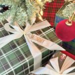 Wrapped gifts with personalized name ribbons under a lit Christmas tree