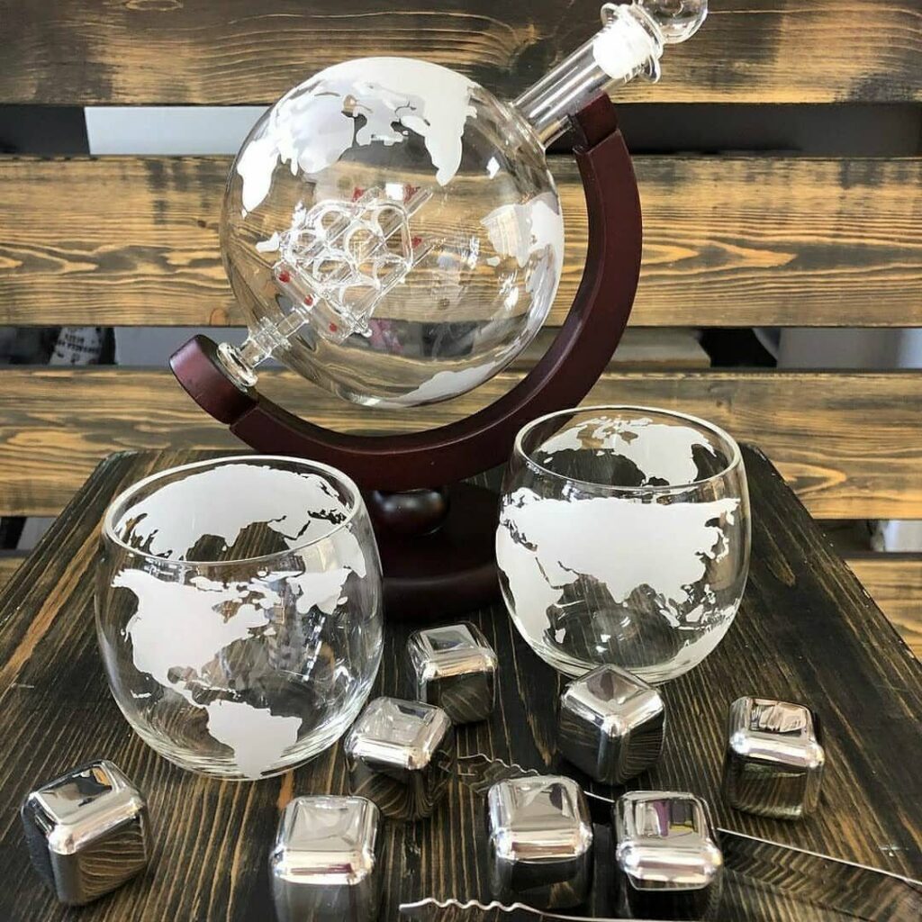 Globe whiskey decanter set with matching glasses and silver chilling stones on wood.