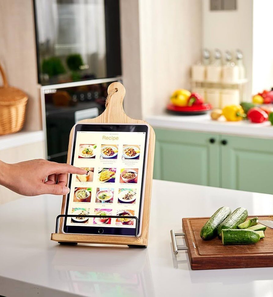 Wooden cookbook stand holding a tablet with recipes on a white kitchen counter.
