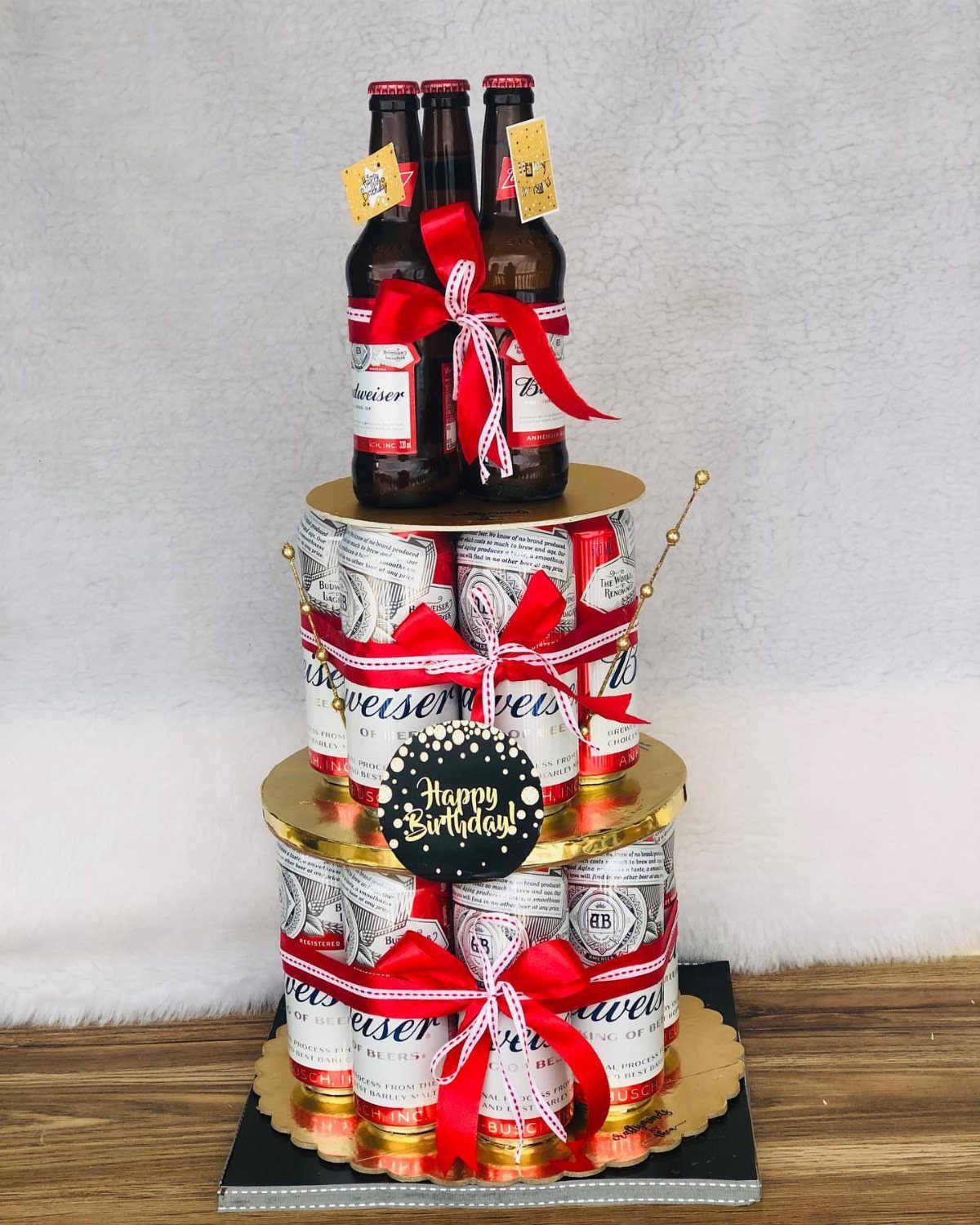 Beer can and bottle cake arrangement with red ribbons and birthday topper.