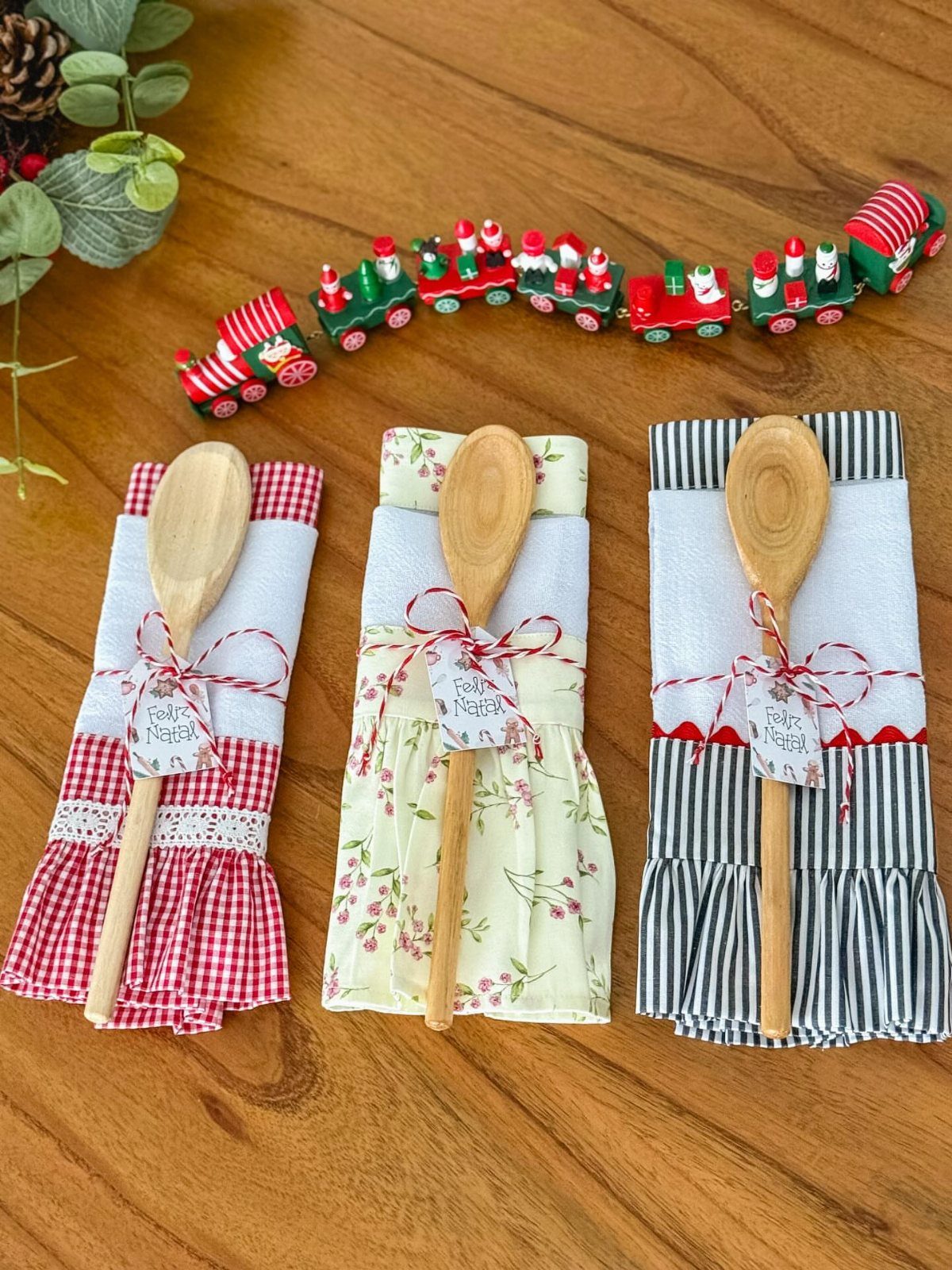 Three patterned dish towels tied with string and wooden spoons on wooden table.