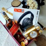 Gift box with scotch whiskey, JBL headphones, Ferrero Rocher chocolates, and roses.