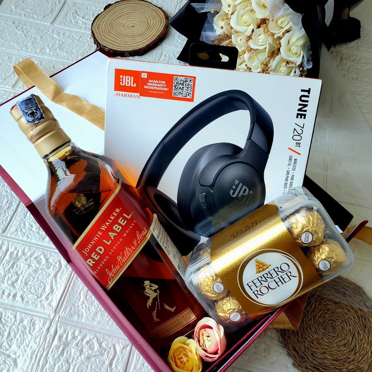 Gift box with scotch whiskey, JBL headphones, Ferrero Rocher chocolates, and roses.