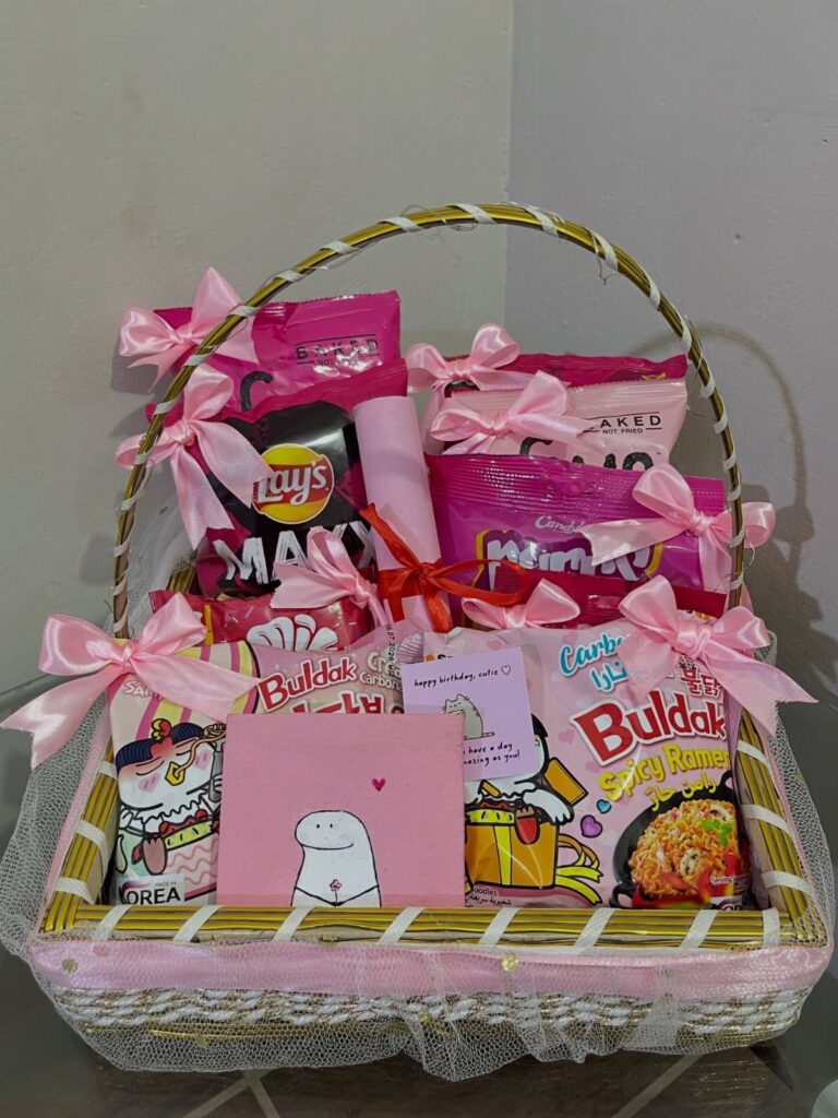 Wicker basket filled with pink snacks and decorated with pink ribbons and cards.