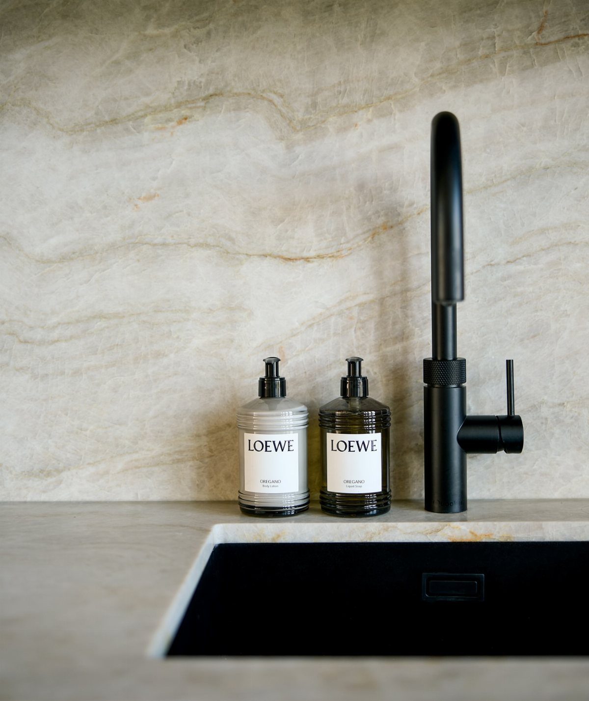 Two Loewe soap dispensers next to a black faucet on a marble counter.
