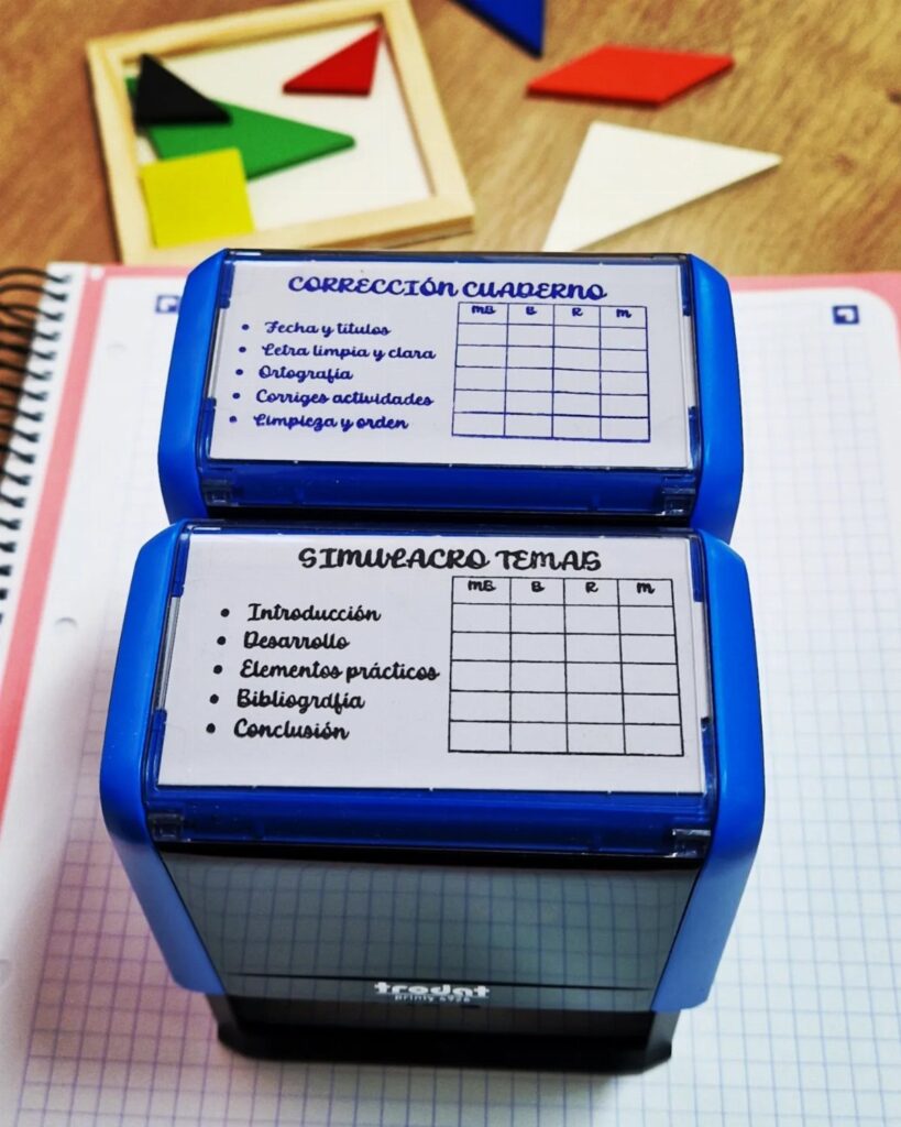Two blue grading stamps with checklists resting on a grid-lined notebook page.