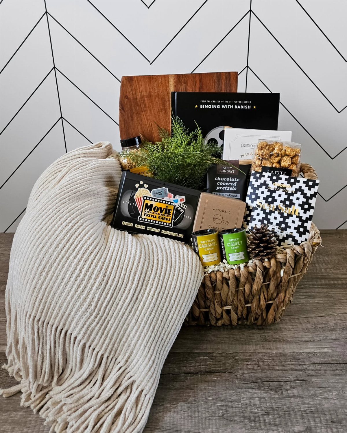 Woven gift basket with popcorn, candy, and a blanket for a movie night.