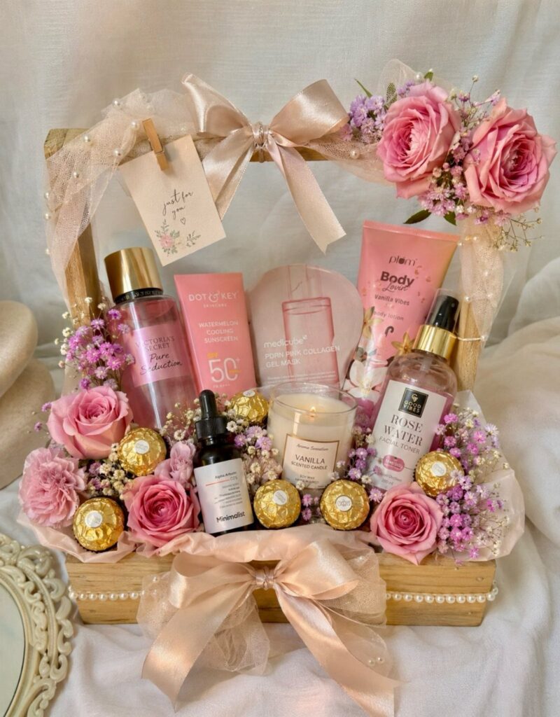 Skincare gift basket with pink beauty products, roses, and gold chocolates in wooden tray
