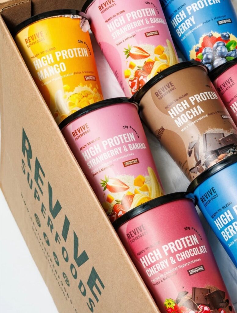 Colorful protein smoothie cans packed inside a cardboard Revive Superfoods delivery box.